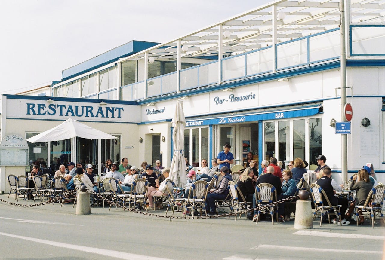 People enjoying a sunny day at a bustling outdoor restaurant in France.